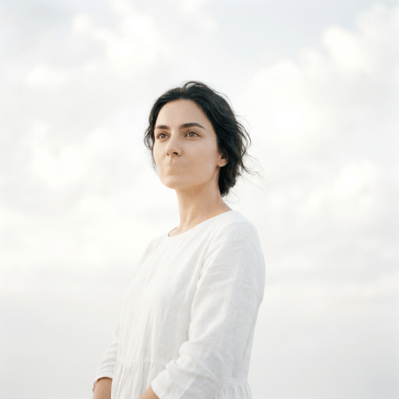 Woman in white gazing thoughtfully against a bright background